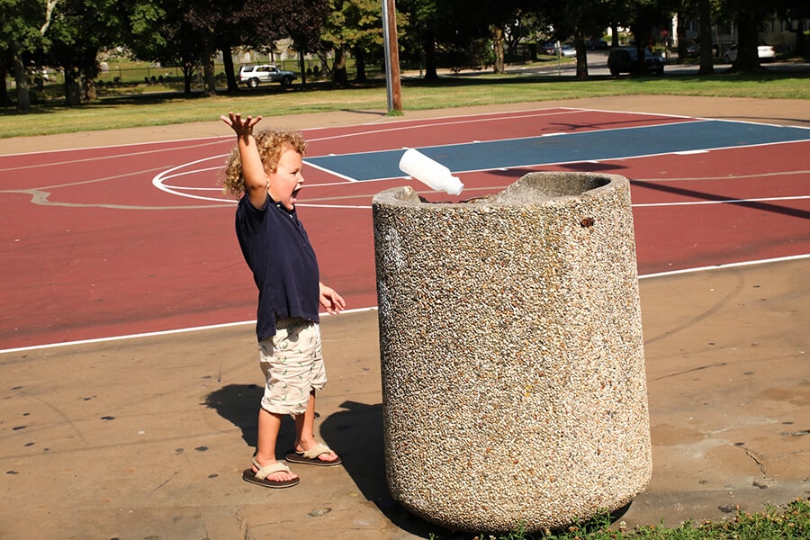 Boy throwing away garbage in a public trash container