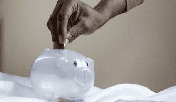 A person putting a coin into a transparent piggy bank. 